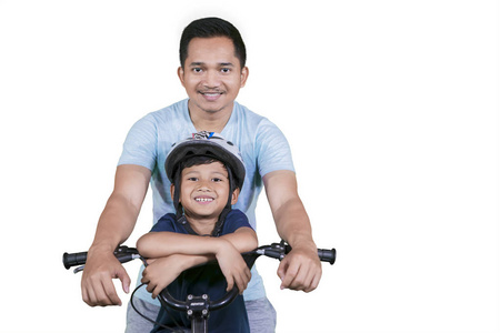 快乐的父亲看着相机，一边骑自行车，和他的儿子在工作室被隔离在白色的背景上