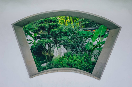 中国杭州西湖附近的一个中国传统园林中,白色墙上开着扇形窗,可以看到