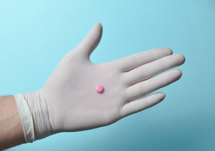 医生手上的粉红色药片，蓝色背景上的白色乳胶手套。医疗护理