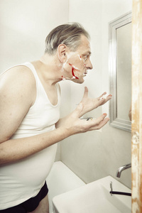 绞尽脑汁一个穿着衬衫的老人刮脸,用老式剃刀割伤自己照片