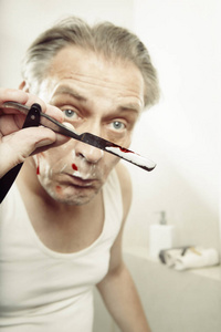 一个穿着衬衫的老人刮脸，用老式剃刀割伤自己