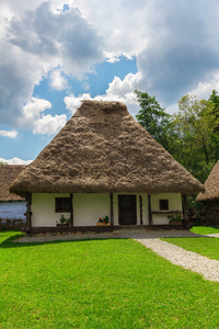 传统的罗马尼亚旧乡村房子，屋顶有茅草，背景有晴朗的多云蓝天