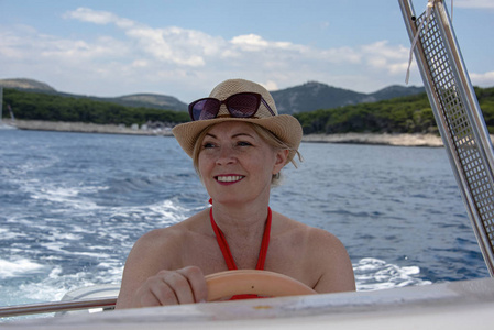 s driving a small boat.  She wears a red dress and hat hat and s