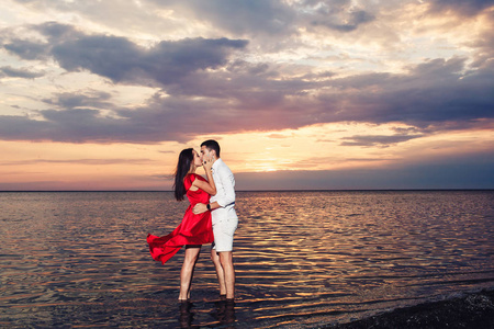 一对恋爱中的年轻夫妇在美丽的日落背景下, 亲吻在大海中