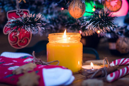 圣诞树下有一支蜡烛在燃烧，旁边有饼干糖果羊毛袜和手套。