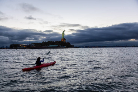 在一个充满活力的多云日出期间，冒险的女孩海在自由女神像附近漂流。摄于美国新泽西州泽西市..