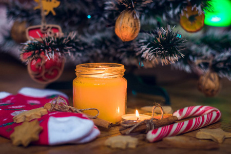 圣诞树下燃烧着一支蜡烛，旁边是饼干糖果羊毛袜和手套。