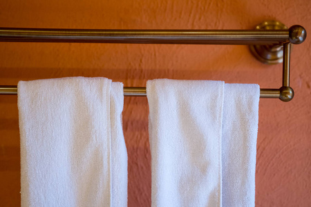 毛巾挂在长不锈钢毛巾架上，靠在橙色的墙壁背景上。
