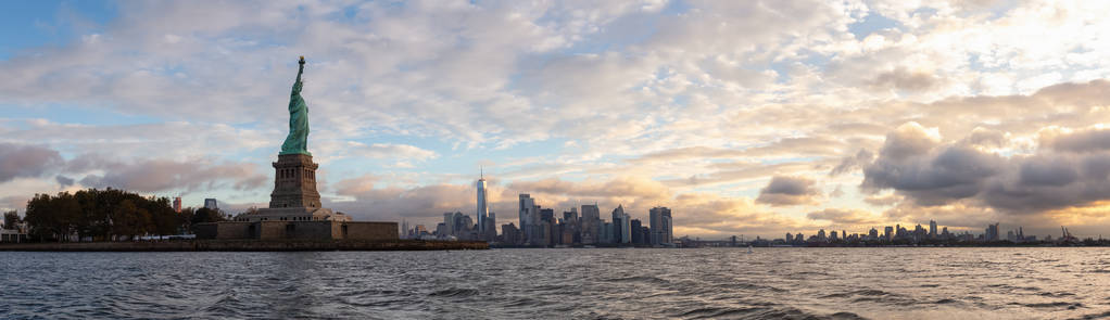 在一个充满活力的多云日出期间，自由女神像和曼哈顿市中心的全景。 摄于新泽西州泽西市，美国。