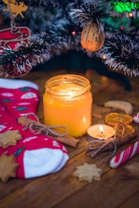 圣诞树下燃烧着一支蜡烛，旁边是饼干糖果羊毛袜子和手套。
