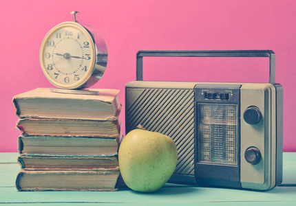 闹钟在一堆旧书上，收音机接收器苹果在粉红色的背景上。 仍然是