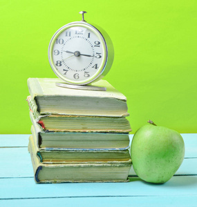 闹钟在一堆旧书上，苹果在黄色的背景上。 学校观念教育
