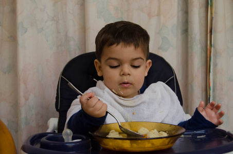 一岁半的男婴在高椅子上用勺子吃汤