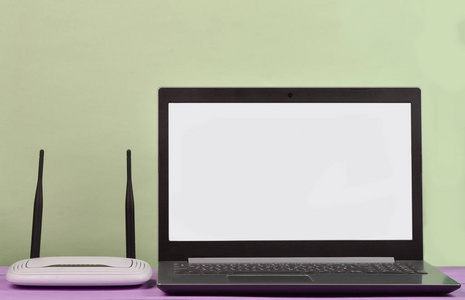 无线路由器白色笔记本电脑屏幕在一张木桌上靠在粉墙上。 复制空间极小