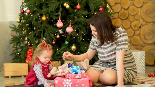 快乐的母亲和她的小女儿在圣诞树附近玩耍。美丽的母亲和她的小女儿坐在节日圣诞树附近的椅子上玩耍