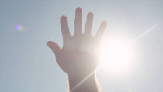 手的特写镜头伸手去拿太阳。股票。明亮的阳光穿过伸出的手的手指向天空