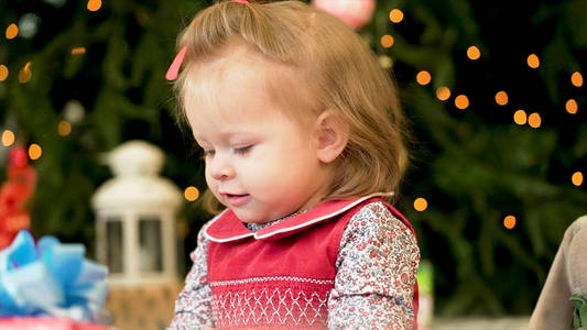 非常漂亮迷人的小女孩在红色的 jaket。在圣诞树背景上玩玩具的小女孩