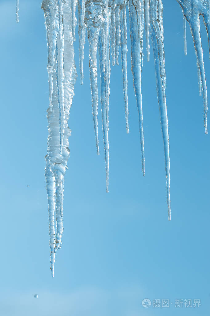 晴空背景上的冰柱. 冰融化和从屋顶坠落对人们来说是一种危险. 水滴.