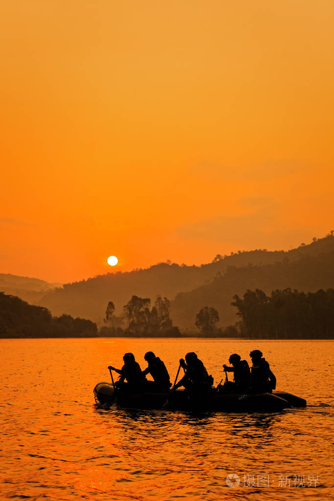 一群士兵帮助划船瞄准黄昏,山和太阳在背景.