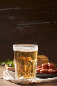 啤酒杯和烤香肠，木桌上放着玉米