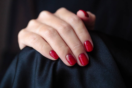 华丽的指甲剪红色指甲油特写照片。 女性手中有深色皮毛背景