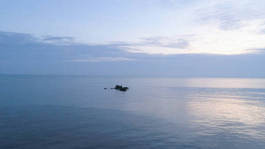 海景，小岩石从水中出来，美丽的蓝色多云的天空。 海上宁静日落的浪漫气氛。