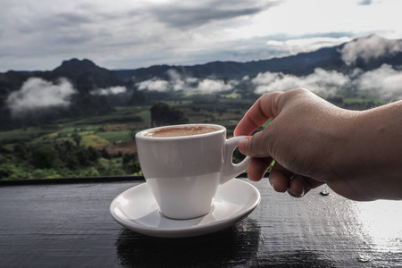 咖啡杯在桌子上，早上有山景作为背景。