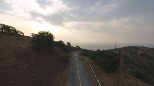 在蛇形道路上的鸟图与美丽的海岸景观与山的背景。拍摄。在日落时绿色沿海山路景观飞行与阴霾的顶视图