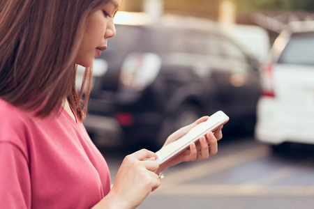 女性使用智能手机应用于汽车模糊背景。 数字技术在日常生活中的概念。