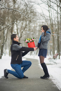 男性用鲜花和女友跪戏剧性的天空风光与崇拜者拟议的男人对女人的婚姻