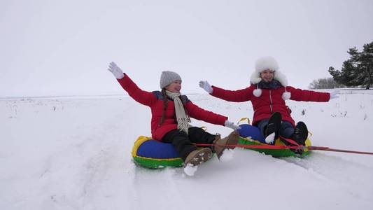 孩子们在雪中滑行在一个充气的雪管和波的手。快乐的女孩骑着雪橇在雪地上滑行。孩子们在公园里玩圣诞节假期在冬天