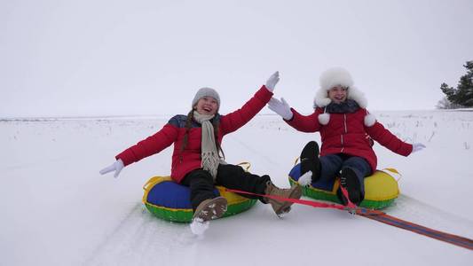 孩子们在雪中滑行在一个充气的雪管和波的手。快乐的女孩骑着雪橇在雪地上滑行。孩子们在公园里玩圣诞节假期在冬天