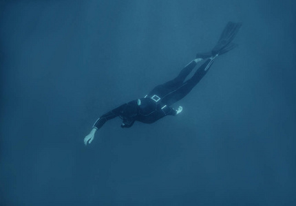 穿着潜水服在水下游泳的活跃的年轻男子自由潜水者。