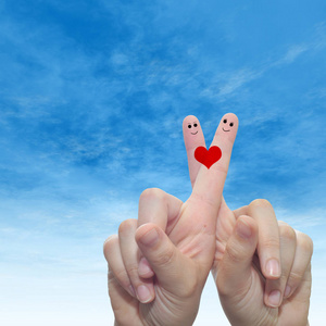 概念或概念人类或女性的双手,用两个手指涂着红色的心,在云蓝色的天空