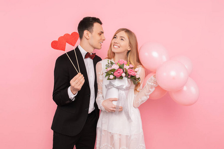 一对相爱的夫妻一个男人捧着两颗纸心，一个女人捧着一束鲜花和气球