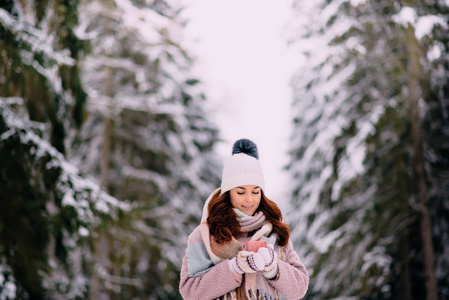 年轻女子手里拿着一杯茶，站在白雪覆盖的公园里