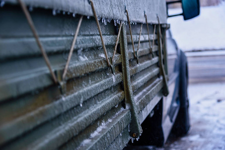 冬天，卡车在一条光滑的积雪覆盖的道路上打滑。一个寒冷的早晨，太阳照进相机，一辆雪覆盖的汽车上的反光镜站在房子附近的停车场里。