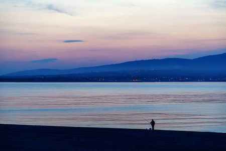 海滩上夕阳中的一个孤独的身影。 戏剧性的晚霞在大海中倒影孤独体贴的倒影