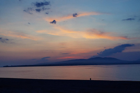 海滩上夕阳中的一个孤独的身影。 戏剧性的晚霞在大海中倒影孤独体贴的倒影