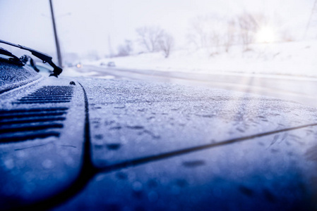 后视镜上一辆雪覆盖的汽车，站在停车场附近的房子在一个寒冷的早晨，阳光照进相机。冬天在积雪覆盖的道路上盖上汽车轮胎。