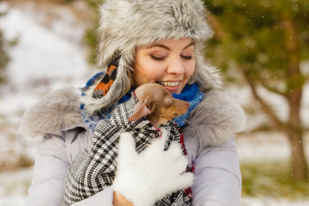 年轻的女人用温暖的毯子围巾包裹她最好的朋友小狗，在寒冷的雪冬天温暖他。 动物保护拯救。 采纳概念