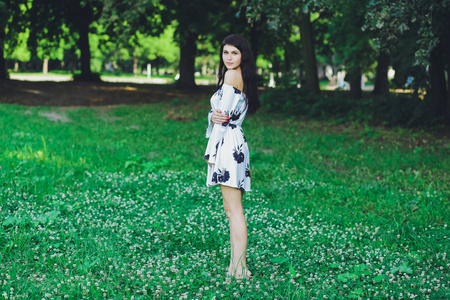 一个年轻美丽的黑发女孩，穿着白色的裙子，在绿草的背景下的夏天公园里