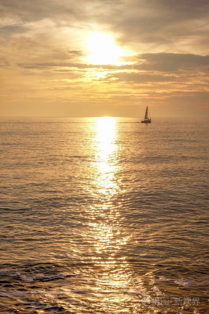 一艘有三个人的帆船在远处剪影在平静的橙色中无缝的大海和天空在黄昏