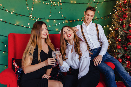 一家年轻的公司，两个女孩和一个男人在家里拿着香槟庆祝新年
