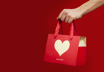 一个女孩拿着一份礼物，在一个孤立的红色背景上做心脏特写。情人节概念。情侣日。