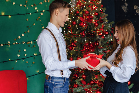 这是一个年轻迷人的女孩，在新年主题圣诞树的背景下，从男人手中接过礼物