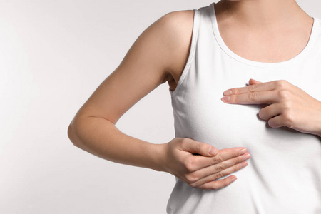 乳腺肿块年轻女子在光线背景下检查她的乳房. 癌症意识概念照片