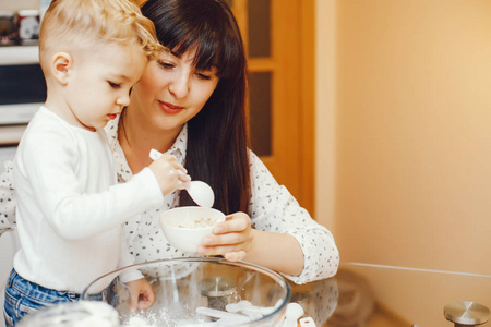 一位穿着白衬衫的年轻母亲正和她的小儿子一起在家厨房准备食物