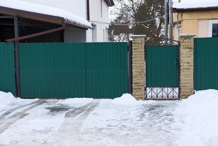 绿色的金属门和白色雪中的栅栏在冬天的街道上漂移