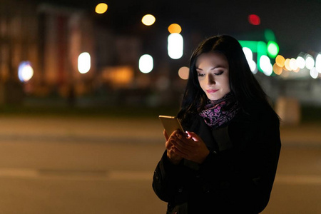 年轻的黑发女人晚上用手机。夜间提供智能电话